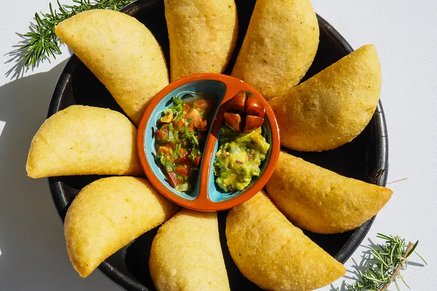 Des empanadas dorées disposées en fleur dans une cazuela noire, autour de deux sauces